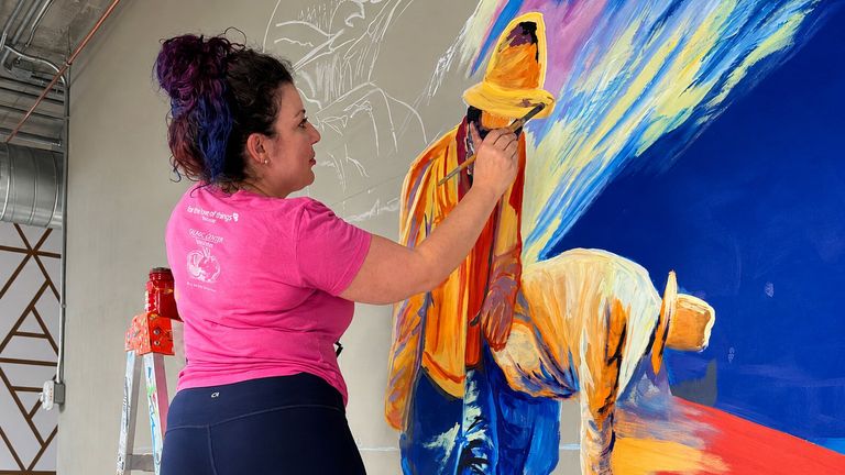 Hayley Ferreira painting a colorful custom mural on an interior wall.