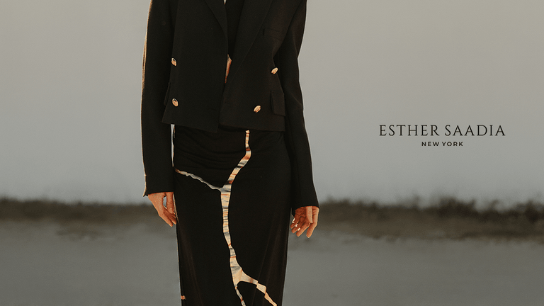 Model wearing a black tailored jacket and flowing skirt with metallic detailing, photographed outdoors for Esther Saadia New York.