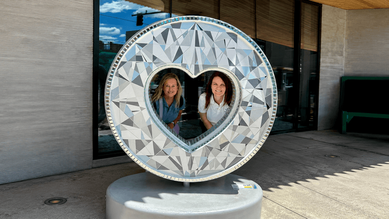 Danielle Marten and Tami Wood pose inside a heart-shaped public art sculpture representing family connection.