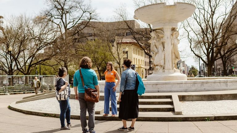 Three people stand around a city fountain, enjoying a moment of connection in an urban setting.