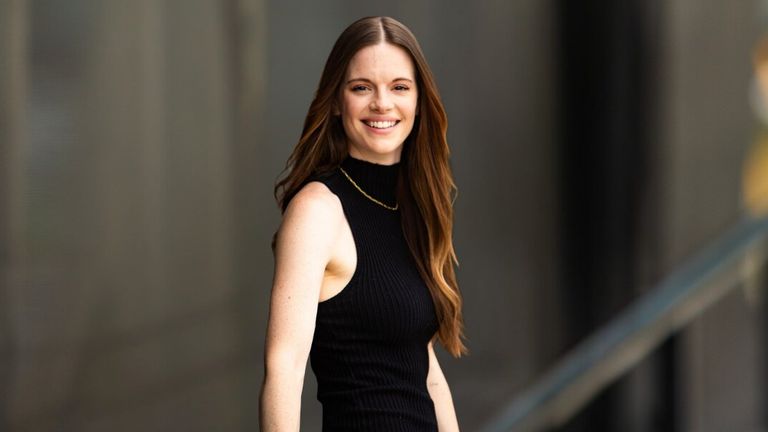 Elle Army is smiling, standing confidently outdoors in a black sleeveless turtleneck, showcasing a compassionate, professional demeanor.