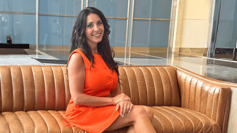 Dr. Cathy Sarvis smiling in a bright orange dress on a couch.