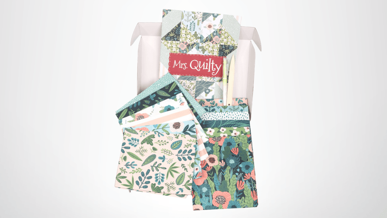 Mrs. Quilty subscription box featuring colorful floral fabric pieces, exclusive patterns, and tools, offering creativity and crafting inspiration.