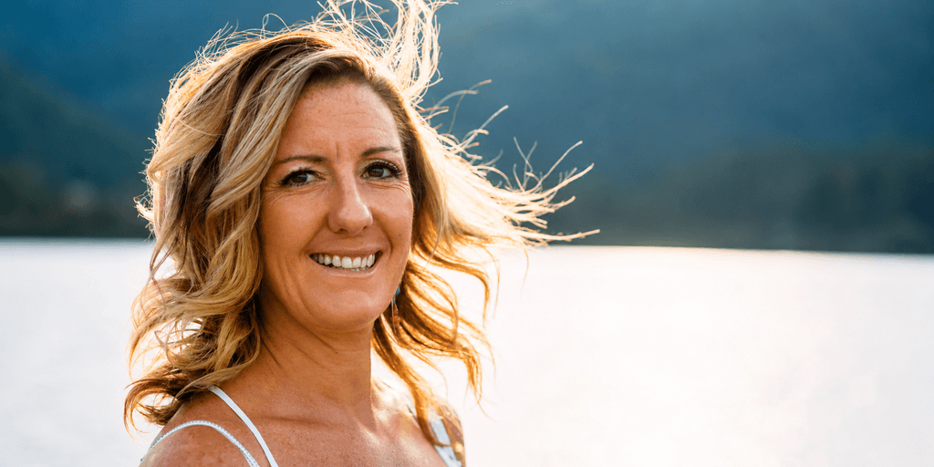 Marjie Martini smiling outdoors beside a lake with mountains in the background.