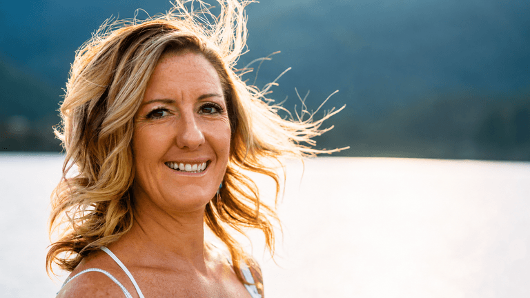 Marjie Martini smiling outdoors beside a lake with mountains in the background.