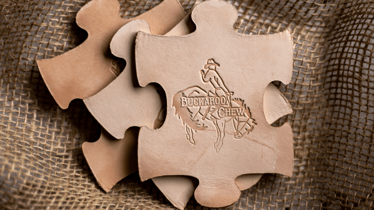 Puzzle-shaped leather pieces with the 'Buckaroo Chew' logo, symbolizing natural, safe teething toys for babies.