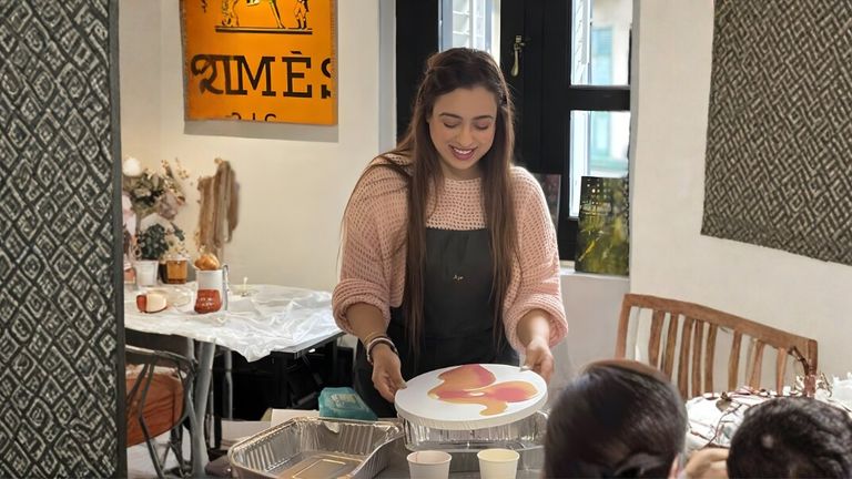 A woman smiling as she presents a painted circular artwork to others in a warm, creative environment.