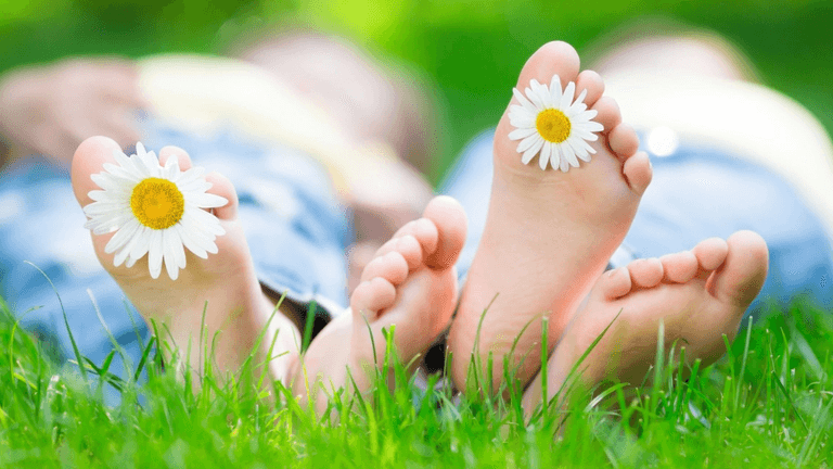 Close-up of feet with daisies between toes, lying on grass.