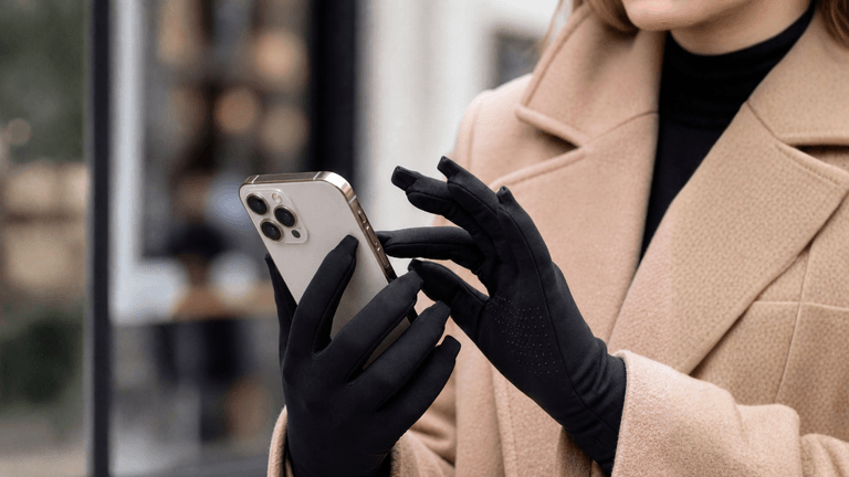 Woman using smartphone while wearing black touchscreen gloves outdoors.