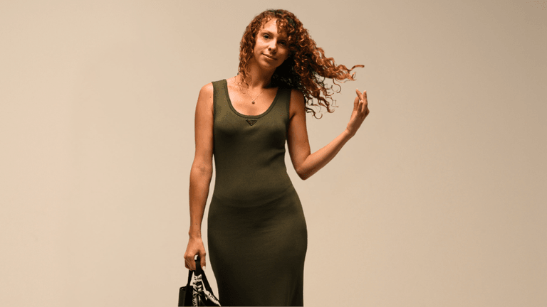 A confident woman in a green dress, holding a handbag, with curly hair flowing.
