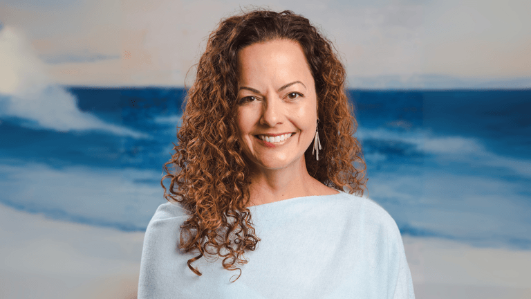 Julie Speetjens smiling in front of ocean background, representing her healing work with Empaths through Reiki and intuition.