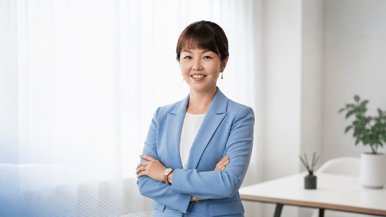 Professional woman in a light blue blazer standing confidently with arms crossed in a modern office.