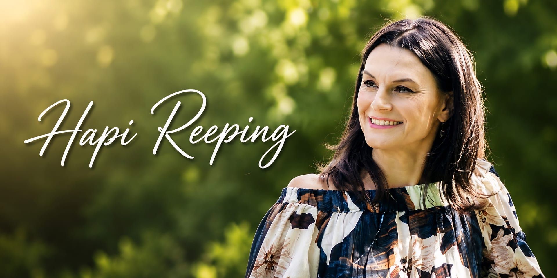 Hapi Reeping smiling outdoors in a floral off-shoulder dress, with “Hapi Reeping” text over a blurred green background.
