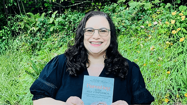 Dr. Jen Ferris smiling while holding her book 'Parenting with Self-Compassion' in front of a green, flower-filled background, promoting her approach to compassionate parenting