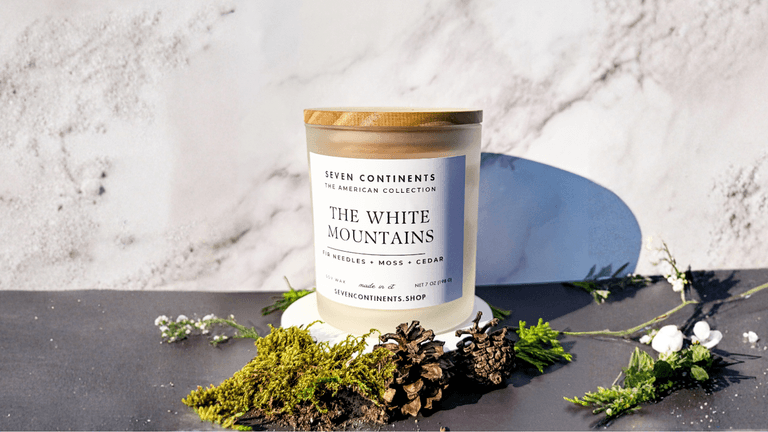The image showcases a Seven Continents candle, "The White Mountains," symbolizing the brand's focus on travel-inspired scents crafted from clean ingredients.