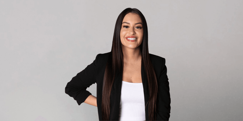 Erica Battista smiling in a black blazer against a neutral gray background.