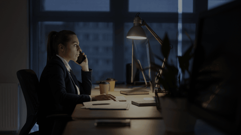 Business professional working late at a desk while talking on the phone in an office.
