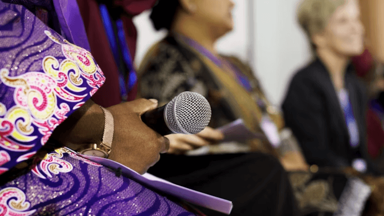 Woman holding a microphone during a panel discussion at a professional women's business event.