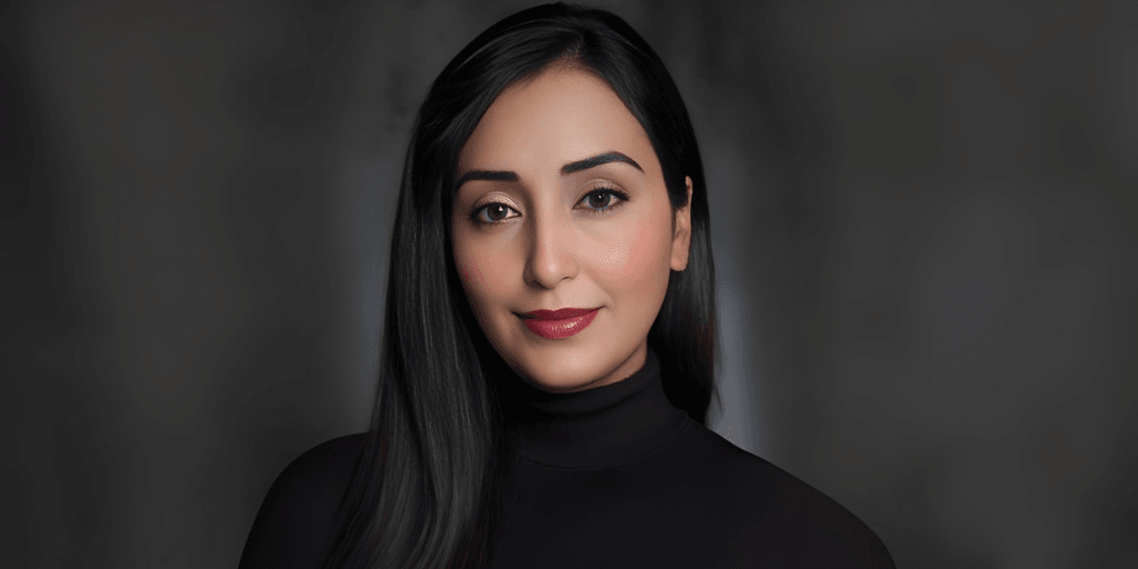 "Portrait of a woman with long black hair and neutral makeup, wearing a black turtleneck top, exuding a professional and confident look against a blurred background."