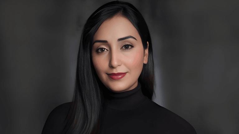 "Portrait of a woman with long black hair and neutral makeup, wearing a black turtleneck top, exuding a professional and confident look against a blurred background."
