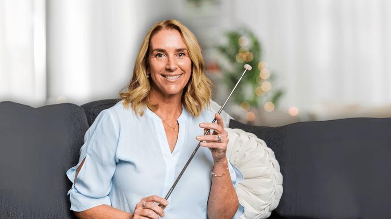Smiling woman sitting on a couch holding a long metal pointer in a softly lit living room.