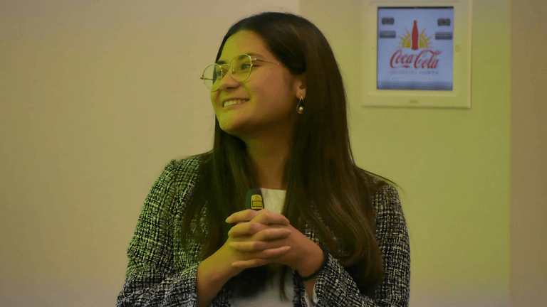Young professional woman smiling and holding a remote control during a presentation, with a Coca-Cola advertisement visible in the background.