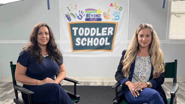 Two women sit in front of a “Toddler School” banner at Beyond Play NYC learning center.