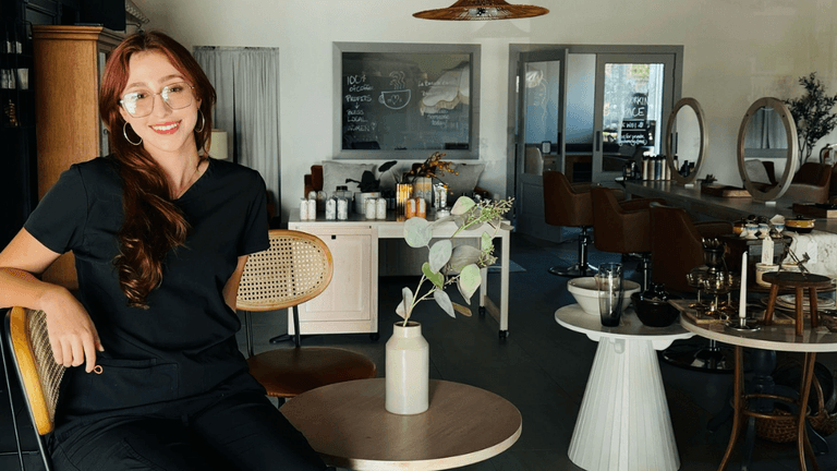 A woman smiles in a modern salon with stylish decor and a cozy, welcoming atmosphere.