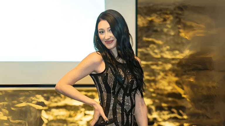 Woman in a black sequined dress posing confidently in front of a presentation screen and textured wall.