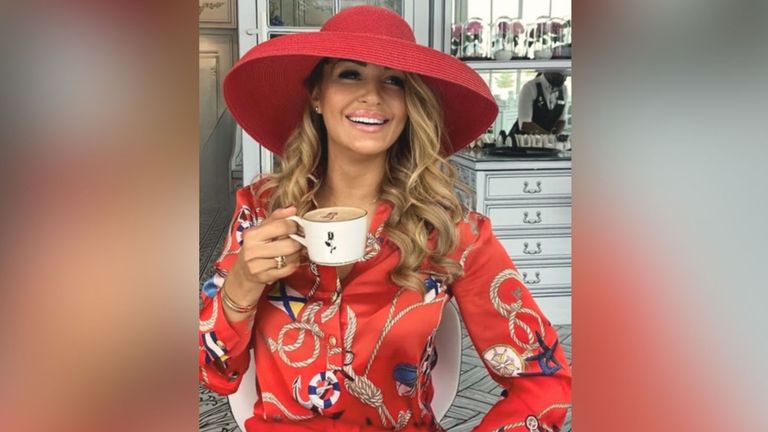 Smiling woman wearing a red hat and a red blouse with a nautical print, holding a coffee cup. She is seated in front of a stylish vanity, creating a chic and fashionable atmosphere."