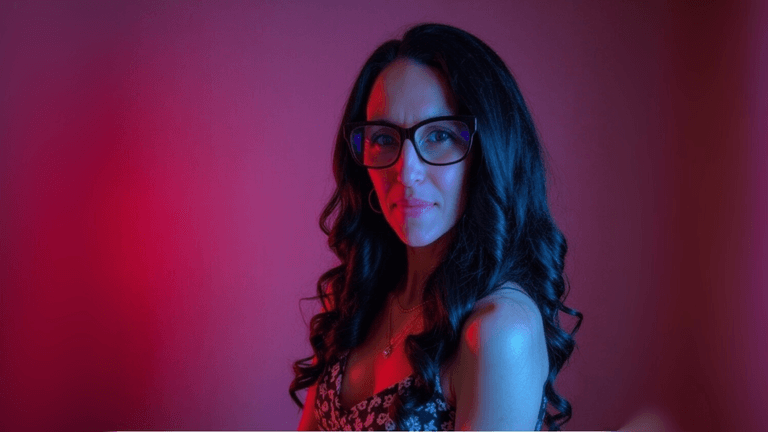 Woman with long dark curls and glasses in colorful lighting, representing Glow Simplicity creator Celeste Marie.