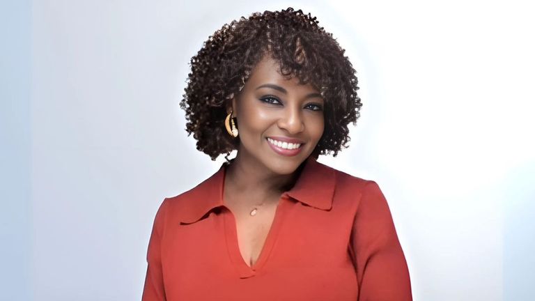 "A woman with curly hair in a red dress smiling at the camera in front of a clean, minimal background."