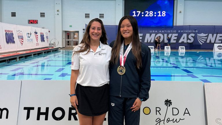 "Irma Davarashvili, artistic swimming coach, poses with her athlete, Isabella Wang, a gold medalist at the 2025 Junior Olympics, celebrating their success at the event in a professional pool setting."