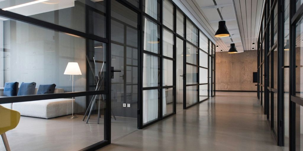 Modern commercial office interior with glass-walled rooms, black framing, pendant lights, and an open hallway.