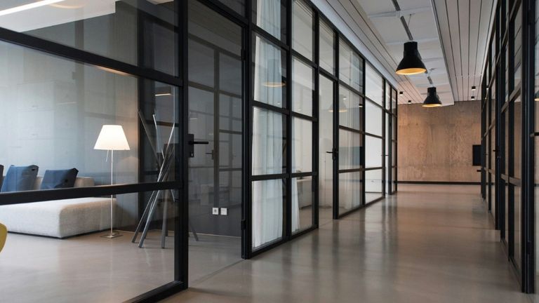 Modern commercial office interior with glass-walled rooms, black framing, pendant lights, and an open hallway.