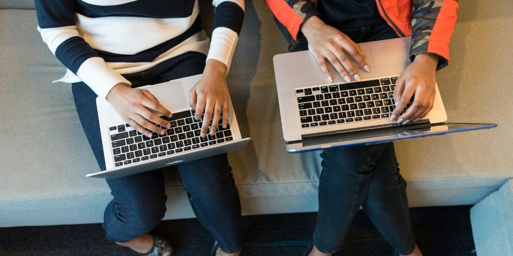 Two people seated side by side using laptops on their laps.
