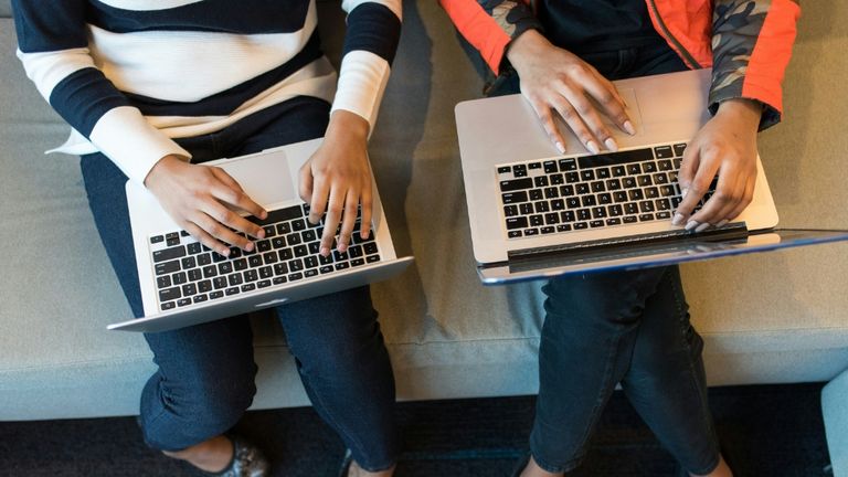 Two people seated side by side using laptops on their laps.