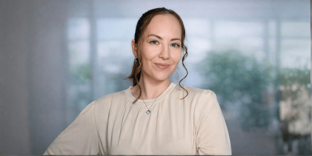 Professional woman smiling in beige blouse with blurred office background.