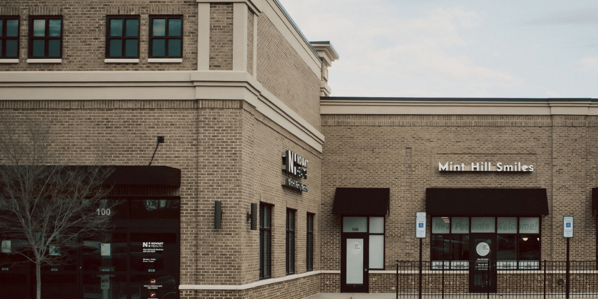 Brick building exterior featuring two storefronts with signs for Mint Hill Smiles and wellness services