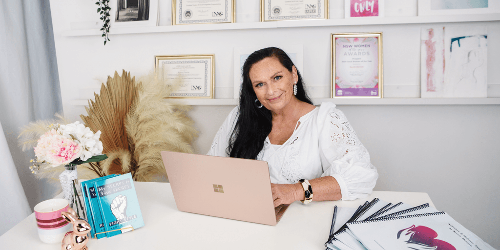 Woman sitting at a desk with awards and notebooks in a bright office setting