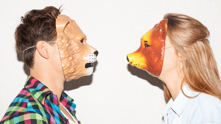 Two people wearing animal masks face each other against a plain background