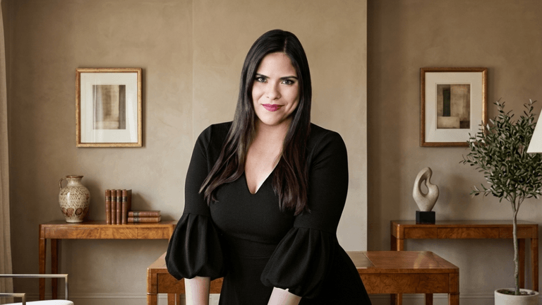 A woman in a black dress poses confidently in a stylish interior setting