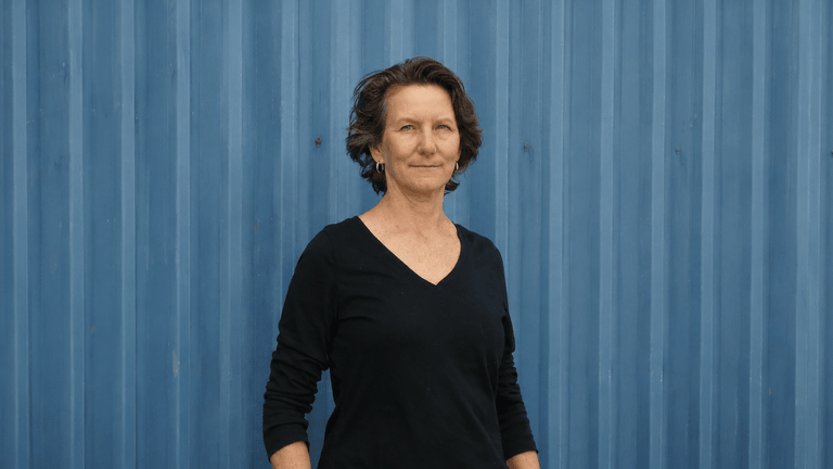 Woman with short hair stands in front of a blue corrugated wall.