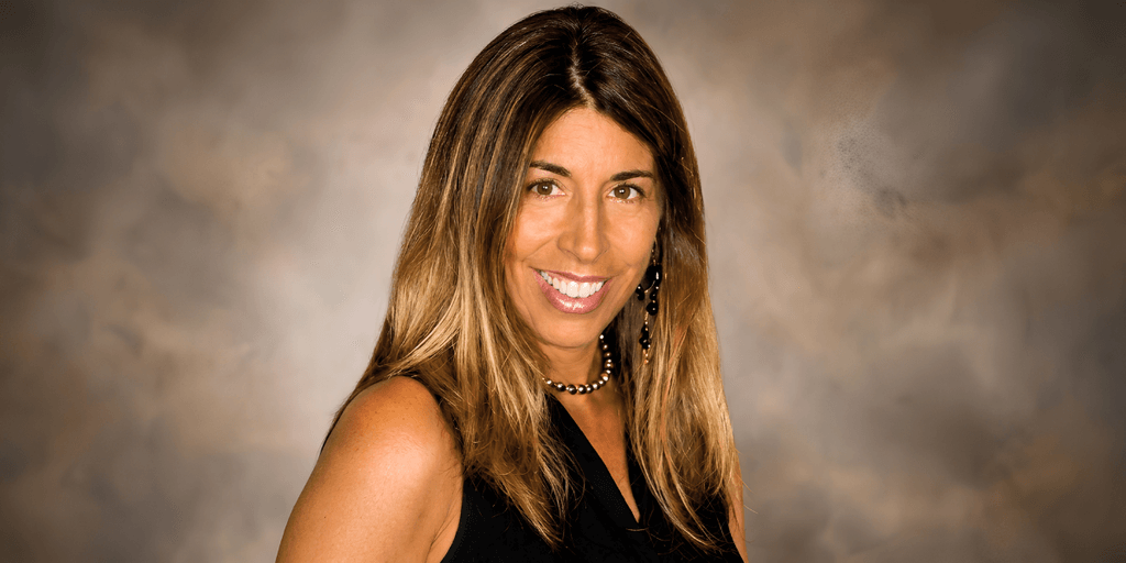 Smiling woman with long, brown hair wearing a black sleeveless top and earrings