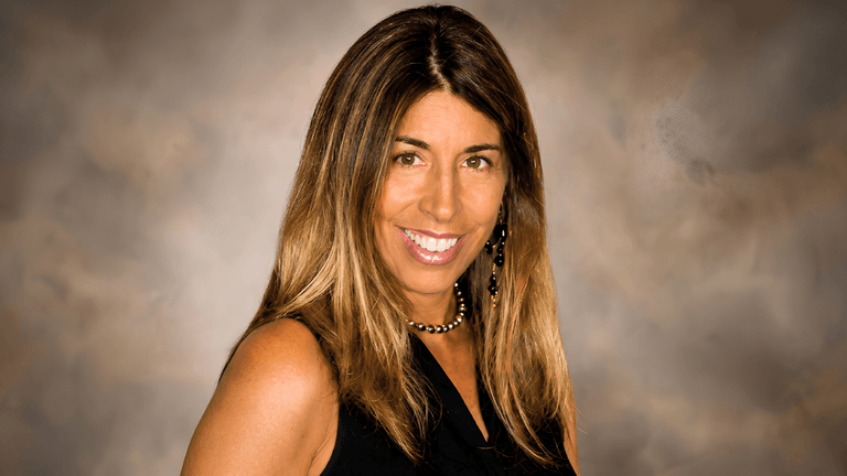 Smiling woman with long, brown hair wearing a black sleeveless top and earrings