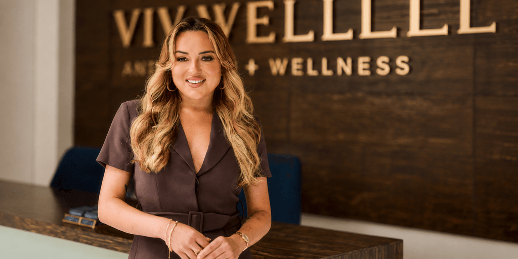 A smiling woman stands at a reception desk in a wellness center