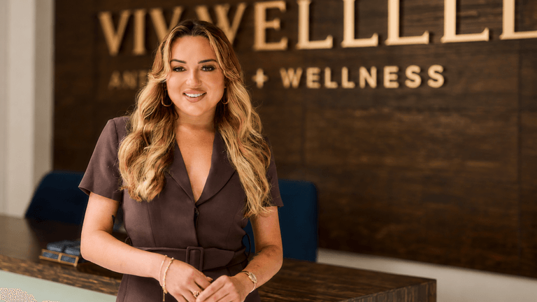 A smiling woman stands at a reception desk in a wellness center