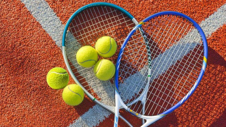 Two tennis rackets and four tennis balls on a clay court surface