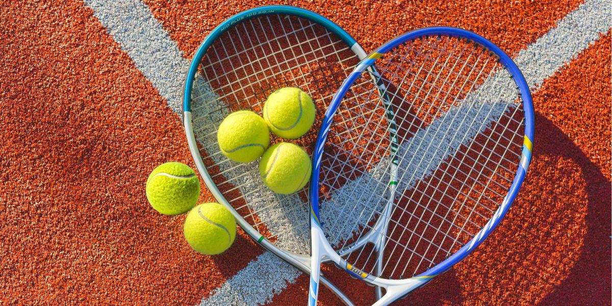 Two tennis rackets and four tennis balls on a clay court surface