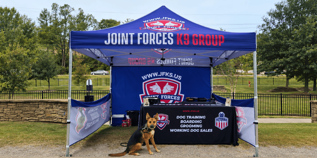 A promotional tent for Joint Forces K9 Group with a dog sitting in front